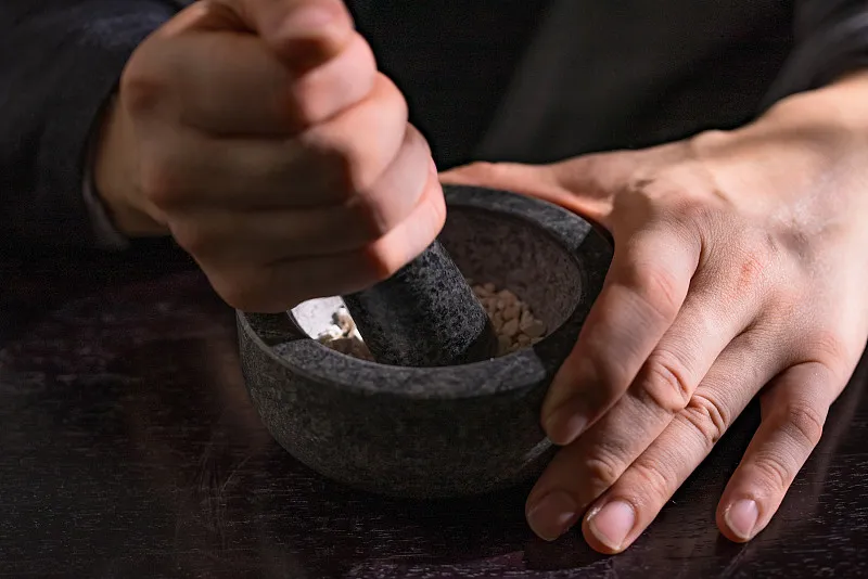 Hands grinding herbs in mortar and pestle—TCM preparation.